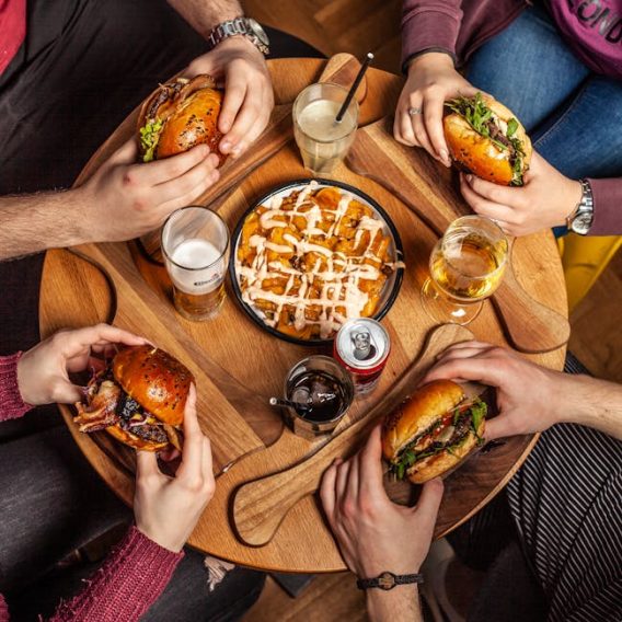 pexels-photo-4809147-4809147 Friends gathered around a table sharing burgers and fries with drinks, creating a casual dining atmosphere.